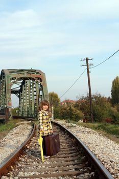 little girl with umbrella and suitcase on railroad