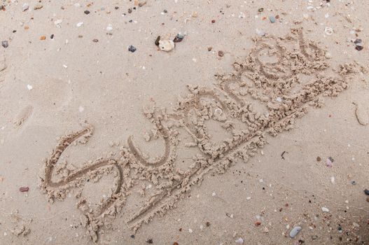 The word summer  handwritten in sand on a beach,