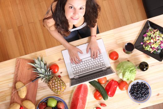 A young woman using a Laptop while cooking.