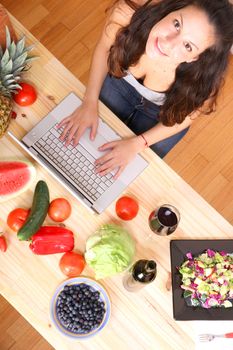 A young woman using a Laptop while cooking.