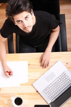 A young hispanic man working on a wooden desk with a laptop.