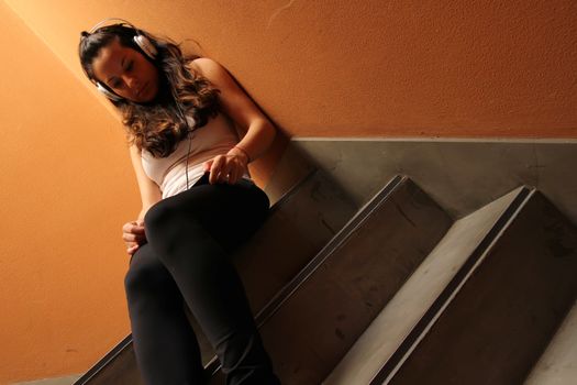 A young woman listening to melancholic Music sitting in the stairway.