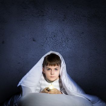 image of a frightened boy under the covers with a flashlight