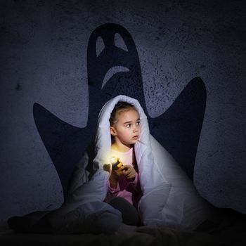 image of a girl under the covers with a flashlight the night afraid of ghosts