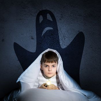 image of a boy under the covers with a flashlight the night afraid of ghosts