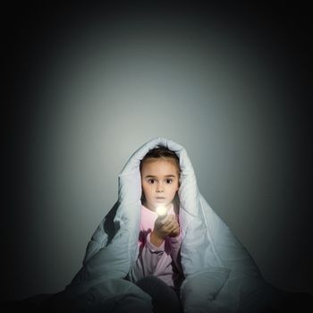 image of a frightened girl under the covers with a flashlight