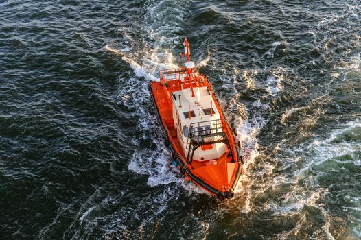 Orange and white coast guard lifeboard photographed from bird's eye-view, visible sunset sunrays, sea and waves.