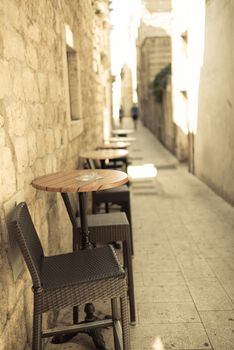 Narrow street of old town with old sandstone buildings, in foreground caffee table and chairs, outdoor photo.