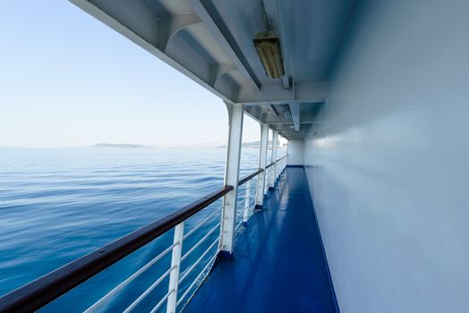Fragment of deck on ship or passenger ferry with visible railing and blue sea, in background cloudless summer sky.