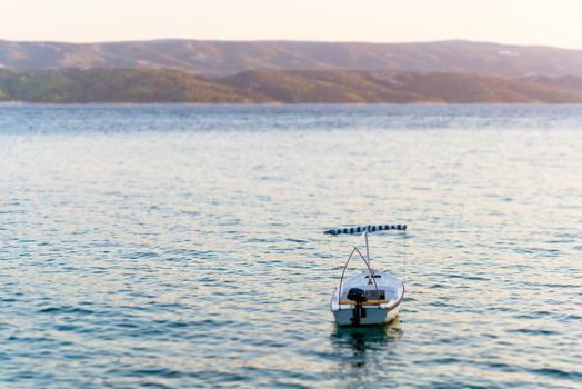 Summer photo of single boat in sea,  in background visible mountains and island coast, illeminated by sun set light, tilt and shift efects.
