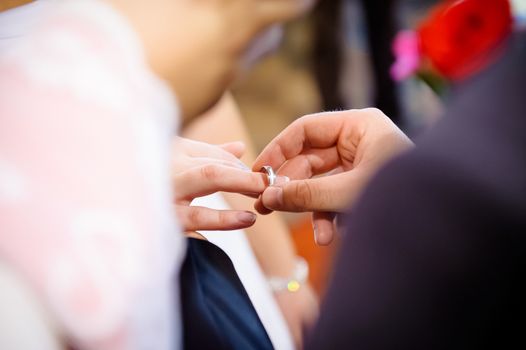 Husband putting wedding ring on on bride's or wife's finger, during wedding ceremony, unrecognizable figures, model release not required.
