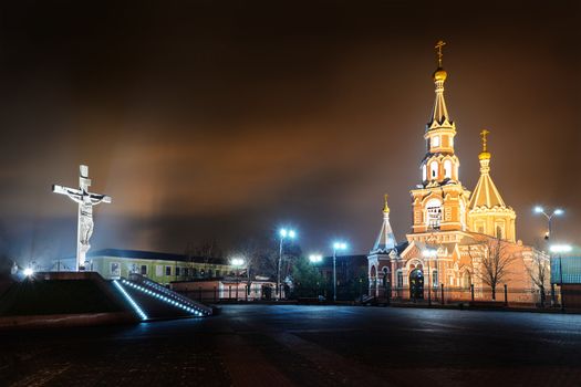 Statue of the crucifixion and church at night. Dniprodzerzhyns'k, Ukraine.