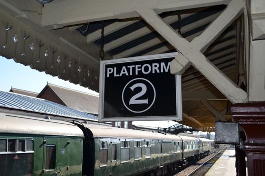 On a restored English Steam railway a platform information sign hangs from the station platform canopy.