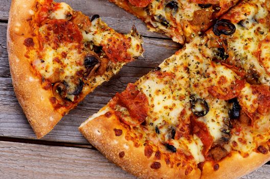 Slices of Freshly Baked Pepperoni Pizza with Black Olives and Spices on Rustic Wooden background. Top View