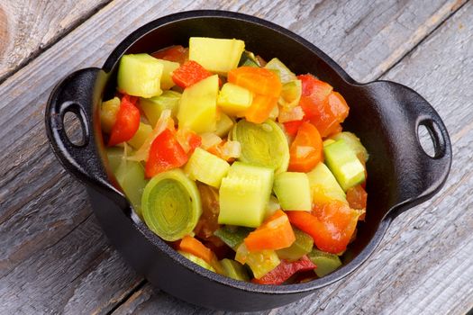 Vegetable Stew with Zucchini and Leek in Black Stew Pan closeup on Rustic Wooden background