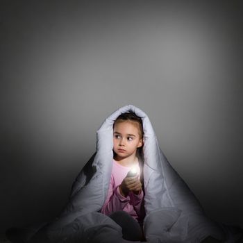 image of a frightened girl under the covers with a flashlight