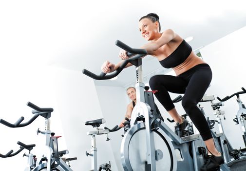 Young athletic female spinning veloargometers in gym, male behind