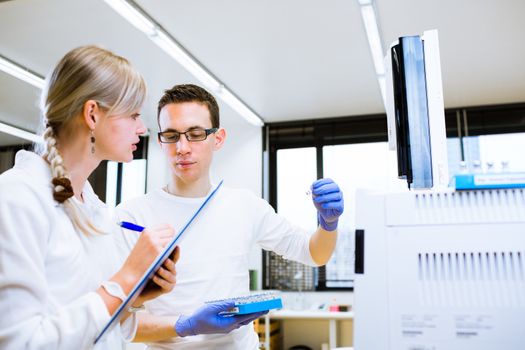 Two young researchers carrying out experiments in a lab (shallow DOF; color toned image)