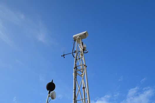 Security cctv camera on a metal pylon under a bright blue sky.