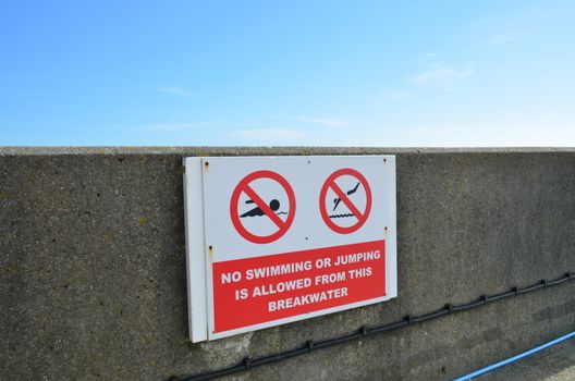 A sign on a sea wall informing the public that swimming and jumping are prohibited.