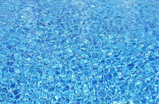 Background of clear water in an outdoor swimming pool with blue tiles.
