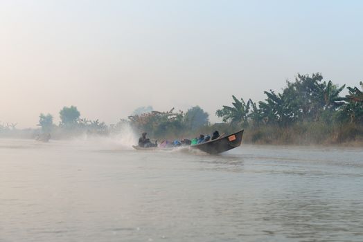 INLE LAKE, MYANMAR (Burma) - 07 JAN 2014: People transportation wooden long boat with motor fast move on blue water in morning fog. Boats is a key transport type on Inle lake. 