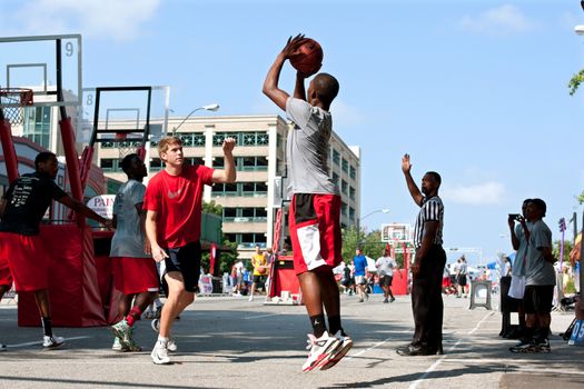 Athens, GA, USA - August 24, 2013:  A young man shoots a jump shot in a 3-on-3 basketball tournament held on the streets of downtown Athens.