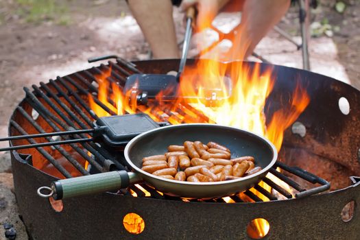 Frying small sausages over an open outdoor fire.