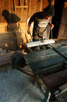 DALAT, VIETNAM- JAN 24: Carpenter saw wood by power saw at home, he working with concentration, his shadow reflect on the wall of wooden house, Viet Nam, Jan 24, 2014                           