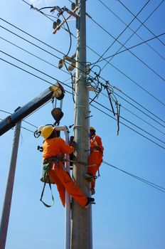 BINH THUAN, VIETNAM- JAN 23: Two electrician repair system of electric wire, they wear safety working clothing, climb and work on electric pole with team under blue sky, Viet Nam, Jan 23, 2014