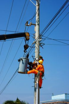 BINH THUAN, VIETNAM- JAN 23: Two electrician repair system of electric wire, they wear safety working clothing, climb and work on electric pole with team under blue sky, Viet Nam, Jan 23, 2014