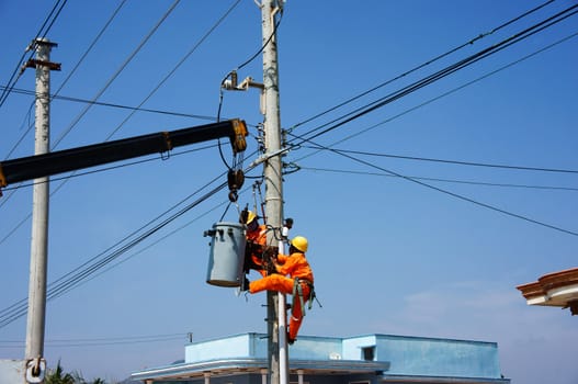 BINH THUAN, VIETNAM- JAN 23: Two electrician repair system of electric wire, they wear safety working clothing, climb and work on electric pole with team under blue sky, Viet Nam, Jan 23, 2014