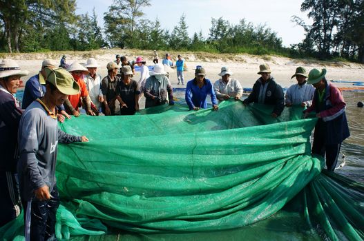 BINH THUAN, VIETNAM- JAN 22: Crowded atmosphere on beach with impression 's group of fisherman pull fish net, row of people with long net in hand, Viet Nam, Jan 22, 2014                           