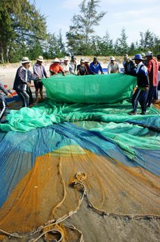 BINH THUAN, VIETNAM- JAN 22: Crowded atmosphere on beach with impression 's group of fisherman pull fish net, row of people with long net in hand, Viet Nam, Jan 22, 2014                           