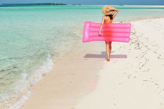 Woman with pink inflatable raft walking at the beach