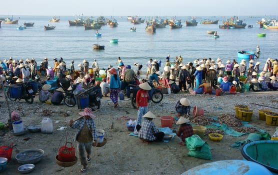 PHAN THIET- VIETNAM- JAN 21: Crowed atmosphere at outdoor seafood market on beach, people trader fishing product in morning, boat on water, man vs woman buy and sell fresh food, Viet Nam, Jan 21, 2014