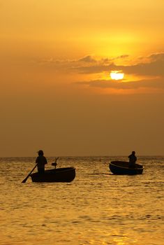 Beautiful landscape on ocean with silhouette of two fisherman standing and rowing on circle boat at sunset, the sun go down, sky in brilliant yellow at sunset