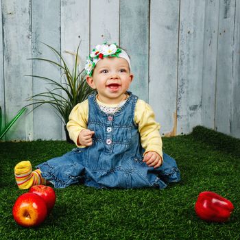 Little girl in the backyard sits on a lawn and smiling at her feet lie apples