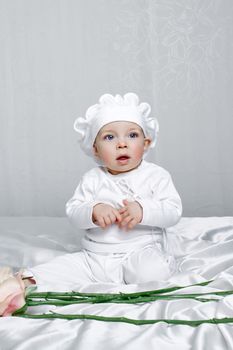 Little girl sitting on silk sheets lie at the feet of flowers