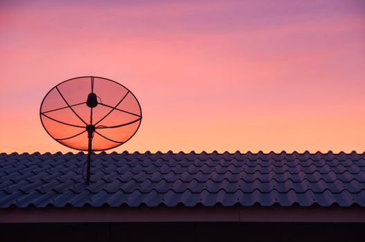 Silhouetted satellite dish on the roof in sunset sky
