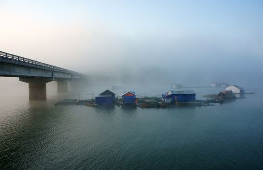 Peacefull landscape of fishing village in fog with hamlet have group of house on surface water, big concrete bridge cross the lake, atmosphere full of misty make romantic of Vietnam country