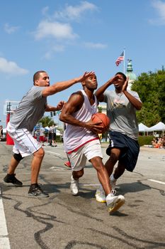 Athens, GA, USA - August 24, 2013:  A young man splits two defenders while driving to the hoop in a 3-on-3 basketball tournament held on the streets of downtown Athens.