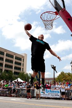 Athens, GA, USA - August 24, 2013:  A young man jumps above the rim to dunk a basketball in the slam dunk competition of a 3-on-3 basketball tournament held in the streets of downtown Athens.