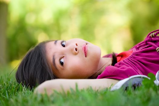 Little girl lying on grass lawn thinking, looking around