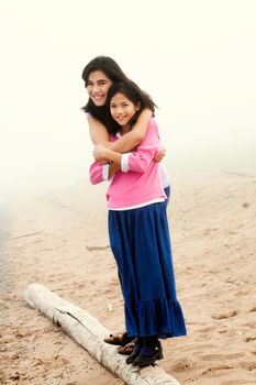 Two sisters hugging on foggy beach