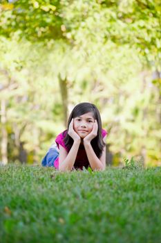 Ten year old girl lying down on grass, chin in hand
