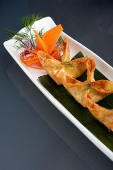 Fried thai crab cream cheese wontons or rangoons appetizer presented on a platter with fancy carrot and herb garnish.
