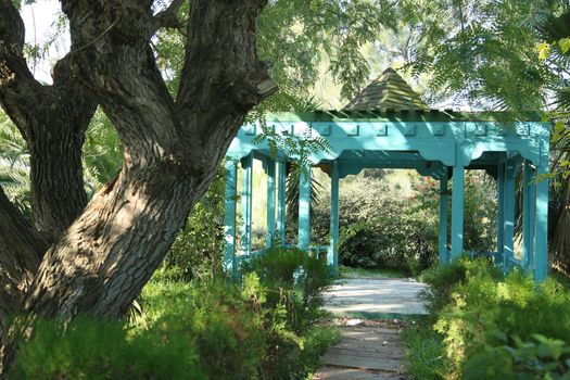 Summerhouse of blue color located in the park and surrounded by greenness