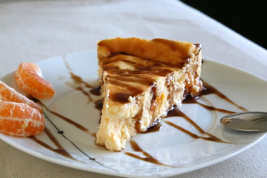 Cheese cake with tangerines and caramel topping. The plate is decorated with three cantles of fresh tangerine.