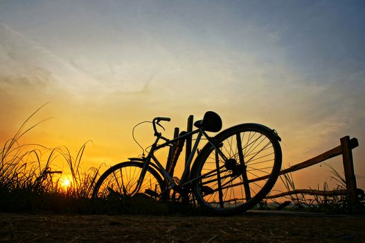 Beautiful landscape of nature with impression 's sun and silhouette of bicycle put up at wooden fence in sunrise at countryside 